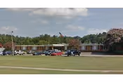 Single-story retirement center building with parked cars, a flagpole, and a front lawn under a partly cloudy sky.