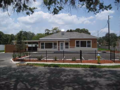 Single-story brick facility behind a black iron fence, with a driveway and landscaped front yard.