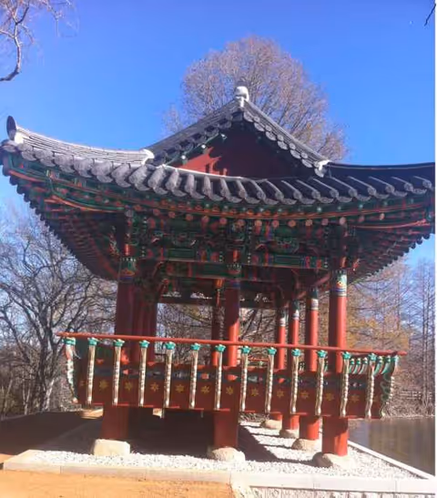 Red ornate pavilion with curved tiled roof in a sunny park.