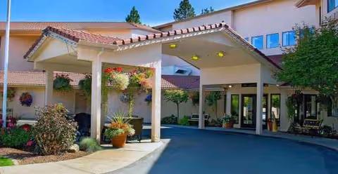 Exterior entrance of Solista Spokane with a covered drop-off, plants, and glass doors.