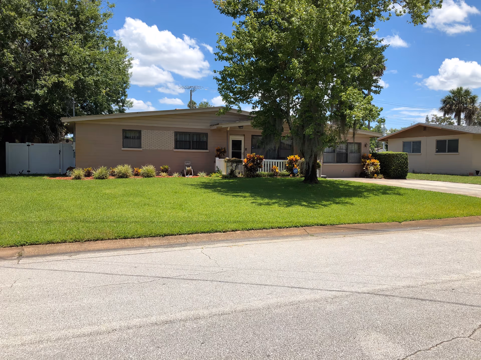 Front view of a single-story ranch-style building with a well-kept green lawn, large tree, and driveway under a blue sky.