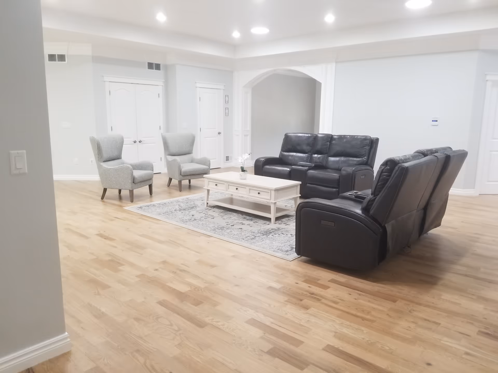 Spacious living room with leather recliner sofas, two gray armchairs, a white coffee table on a rug, and hardwood floors.
