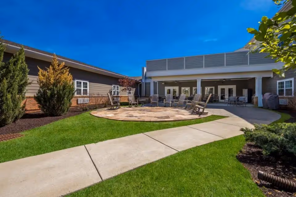 Sunlit courtyard at Traditions of Smyrna with a circular stone patio, rocking chairs, paved walkway and the building façade in the background.