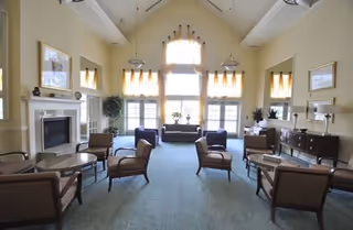 Spacious senior living common lounge with high ceilings, large windows, a fireplace, and arranged seating.