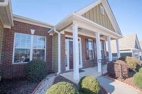 Front exterior of a brick senior living facility with a covered entrance and columns.