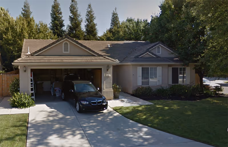 Front exterior of a single-story house with an open garage and parked car.