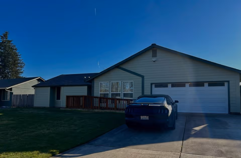 Single-story house with an attached garage, front porch and a car parked in the driveway under a clear blue sky.