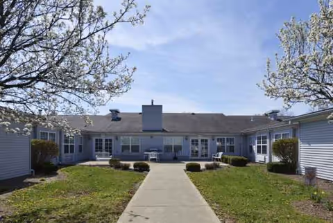 Cardinal Place exterior: a single-story senior living building with central walkway, lawns, and shrubs.