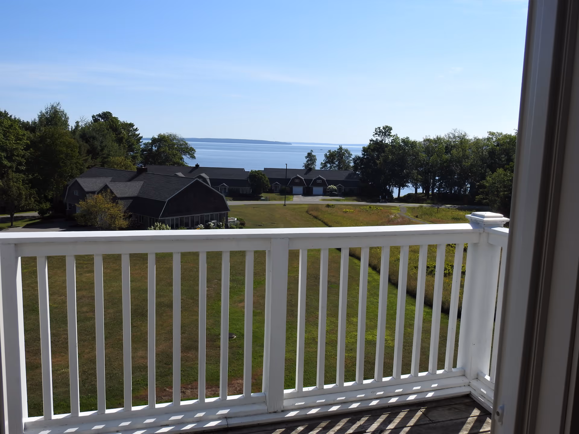 View from a white balcony railing overlooking lawns, residential buildings, trees and a distant body of water.