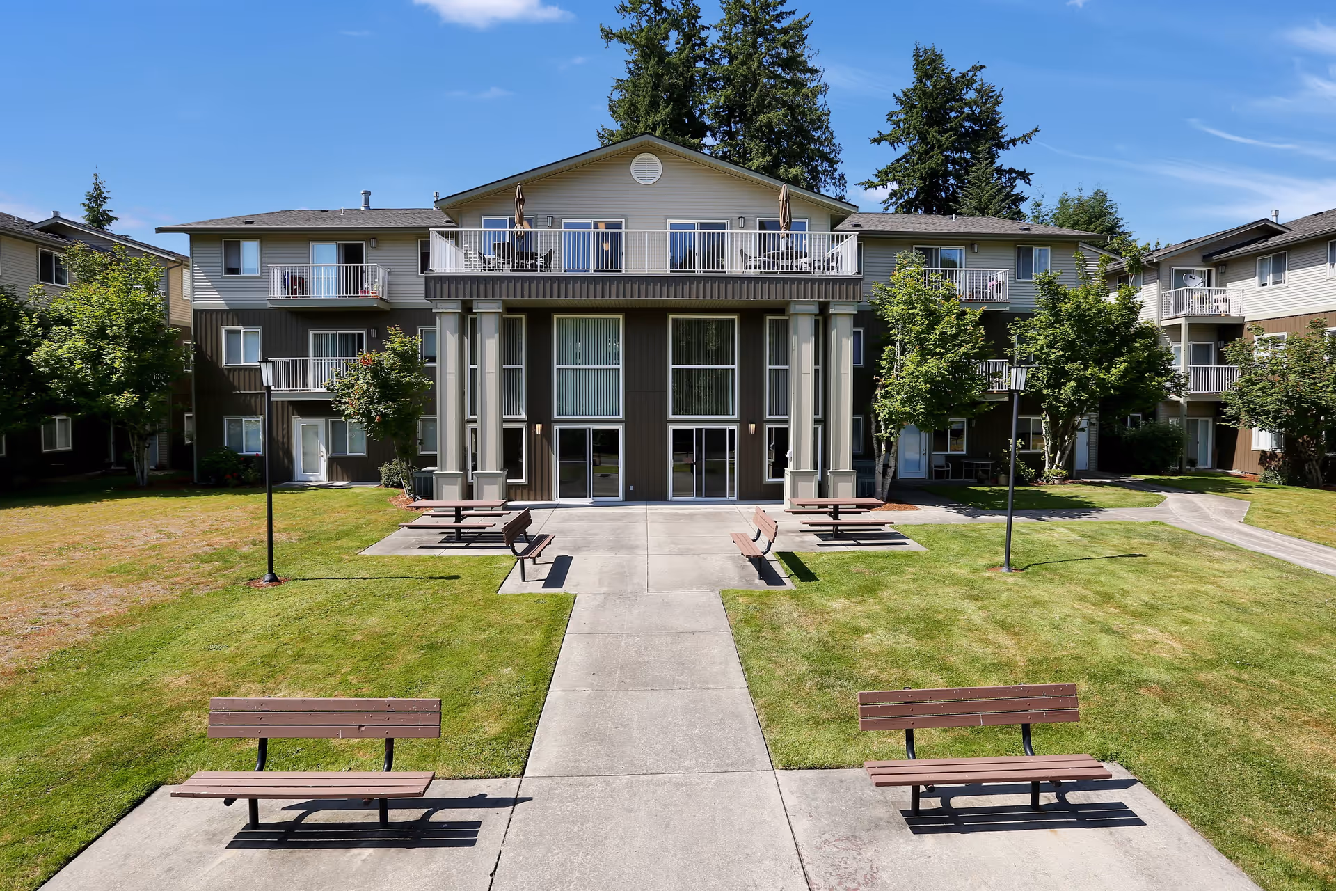 Three-story senior apartment building with balconies facing a grassy courtyard with benches and picnic tables.