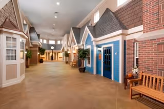 Spacious indoor corridor styled like a village with small house-front facades, benches, and potted plants.