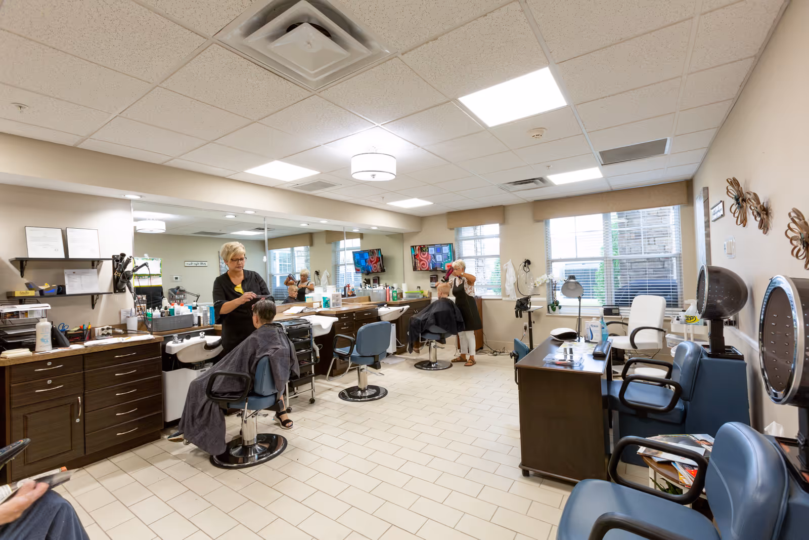 Interior salon with stylists cutting clients' hair at multiple styling stations with mirrors and chairs.