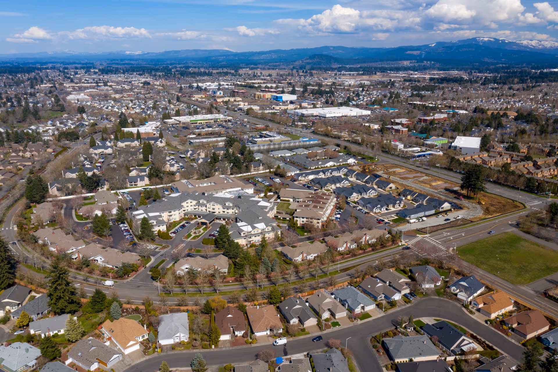 Aerial view of a senior living campus and surrounding suburban neighborhood with roads, houses, and distant mountains.