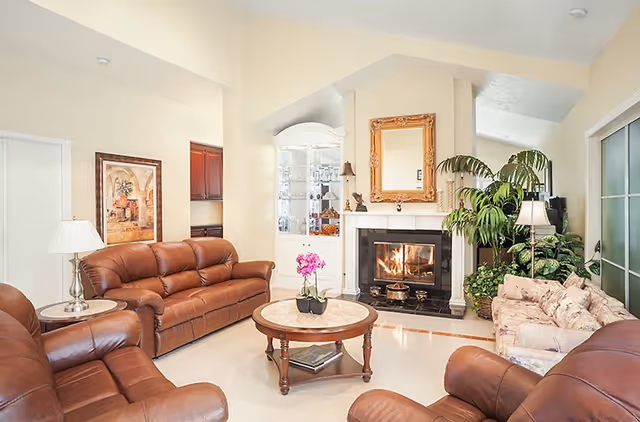 Cozy living room in a senior facility with leather sofas, a fireplace, and plants.