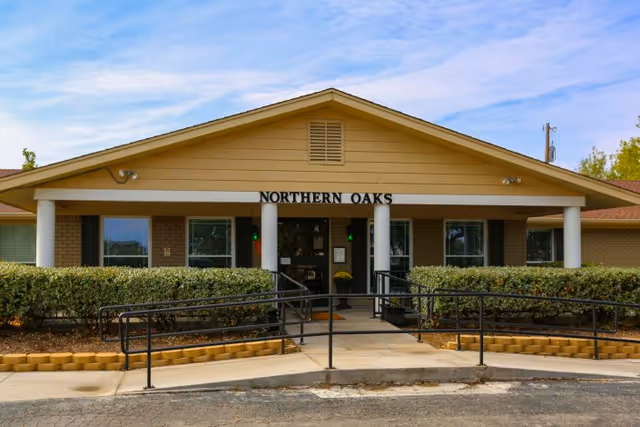 Front entrance of Northern Oaks with a covered porch, columns, wheelchair ramp and shrubs.