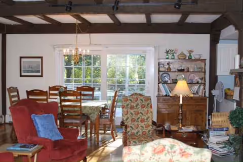 Cozy living room with red armchair, floral chair, dining table, and shelving.
