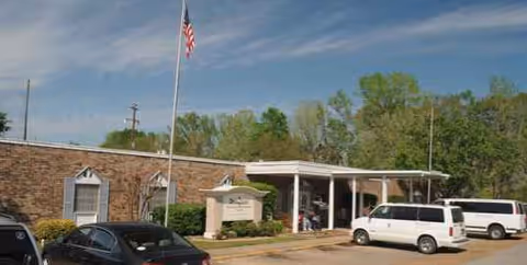Exterior view of Winnfield Nursing and Rehabilitation Center front with flag and parked cars.