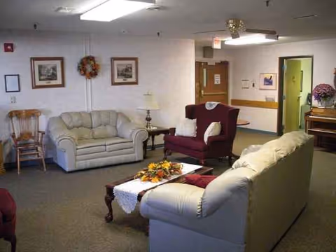 A warmly furnished senior living common area with sofas, chairs, and a coffee table.