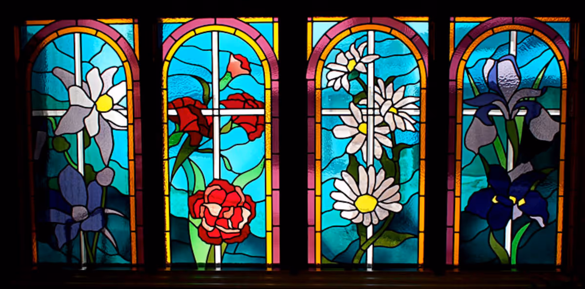 Four stained glass windows each featuring different floral designs with vibrant colors including white, red, yellow, purple, and green on a blue background.
