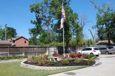 Circular landscaped island with flagpole and cars in front of the facility.