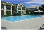 Outdoor swimming pool in front of a two-story residential building with poolside chairs and umbrellas.