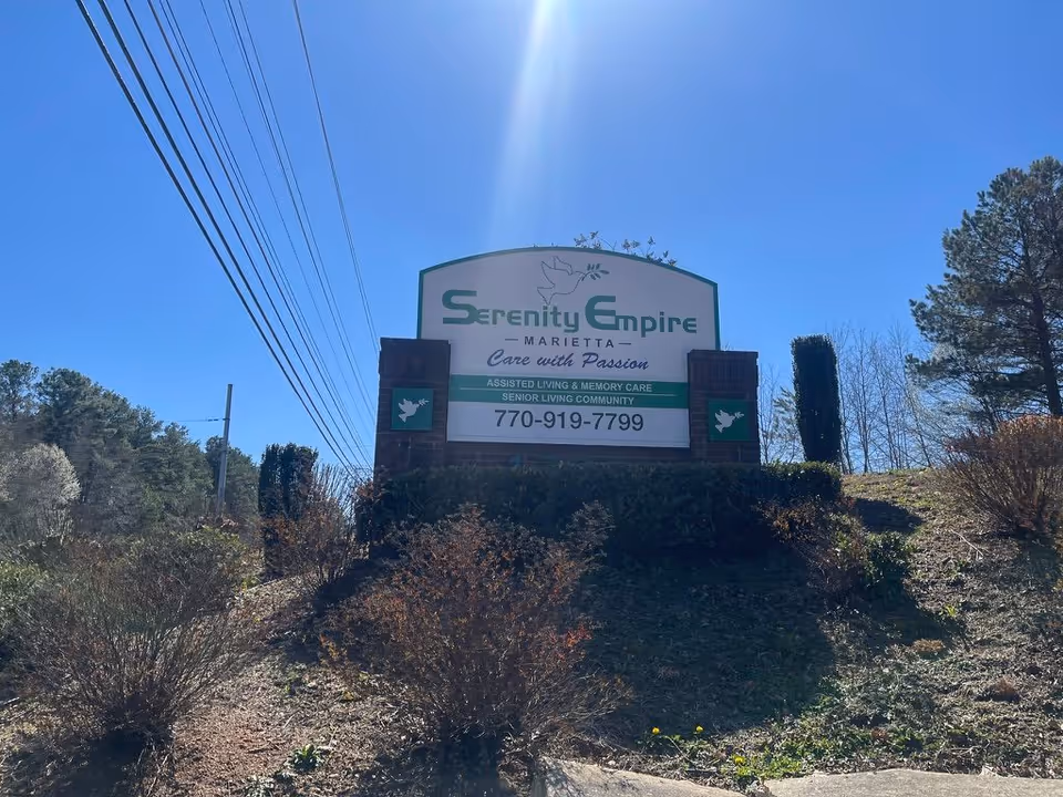 Outdoor sign for Serenity Empire Marietta assisted living community on a landscaped hill under a clear blue sky.