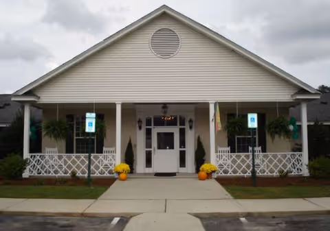 Senior living facility front entrance with white porch, potted plants, and pumpkins.