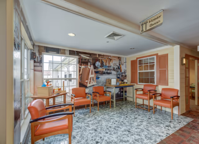 Bright seating area with orange chairs, tables and a large workshop-themed wall mural in a memory care facility.