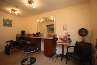Small salon room featuring styling chairs, a countertop with a large mirror and hair-drying equipment.