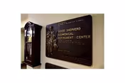 Interior hallway with a large bronze commemorative plaque mounted on the wall and a tall grandfather clock beside it.