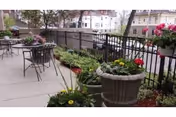 Outdoor patio with metal tables and chairs and several potted flowering plants along a railing.