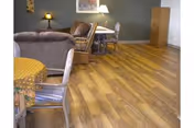 Spacious senior living lounge with wooden floors, armchairs, and tables.