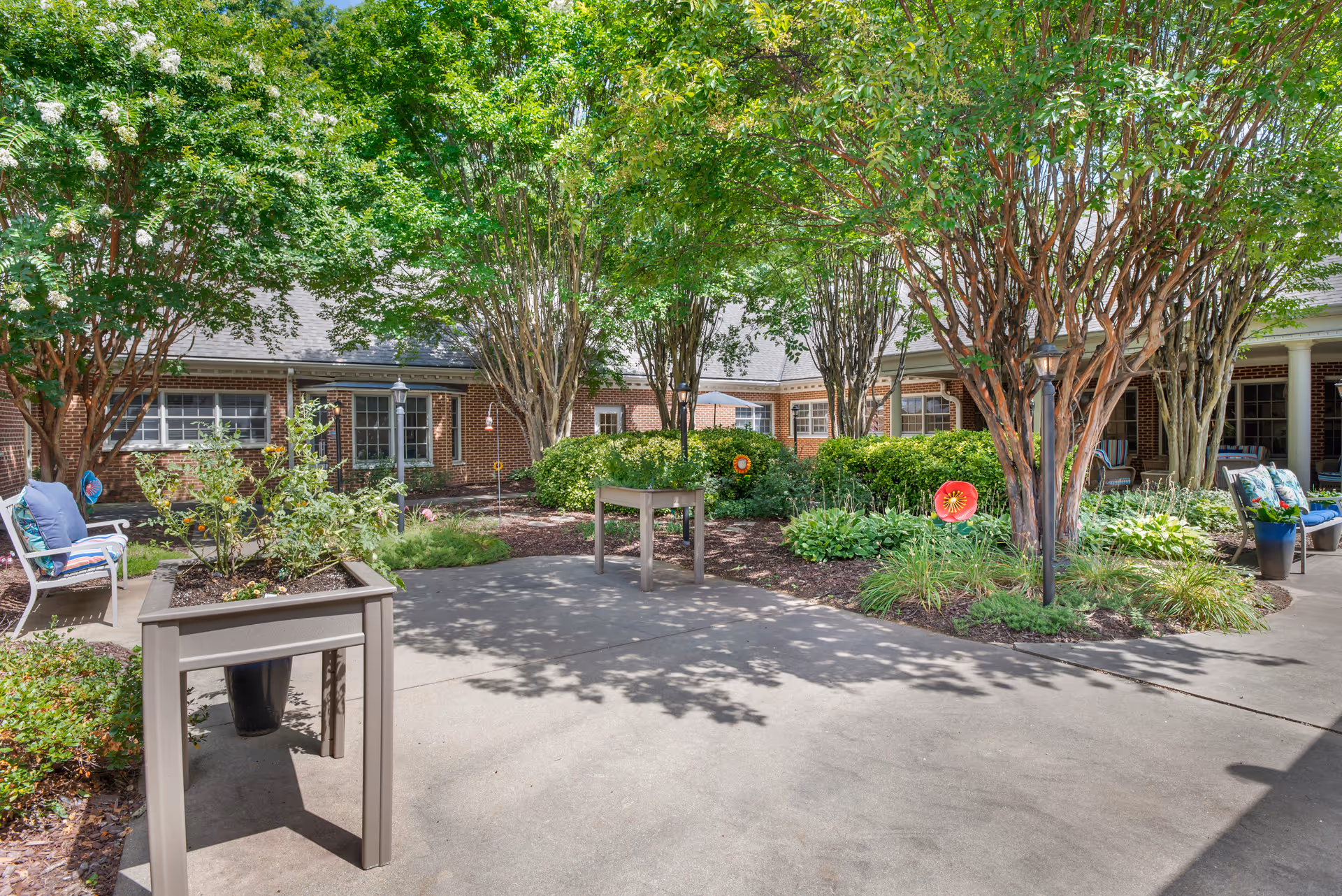 Shaded courtyard with trees, planters, benches and a surrounding brick residential building.