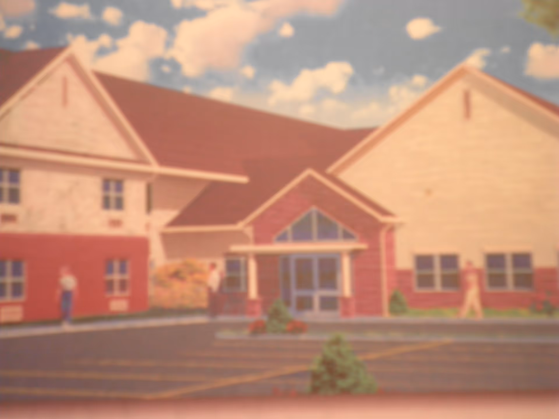 Exterior view of a building with a red roof and beige walls, featuring a central entrance with glass doors and a small covered porch. There are a few people walking near the building, and the sky is partly cloudy.