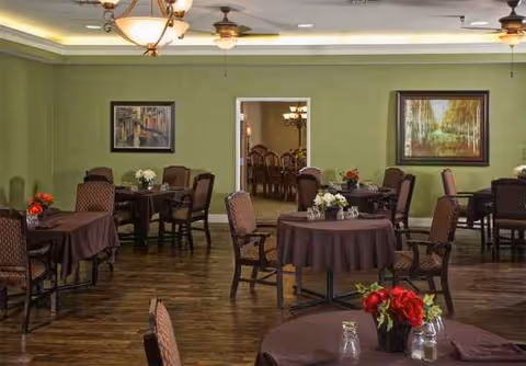 A dining room with brown tablecloths, chairs, and floral centerpieces in a senior living facility.
