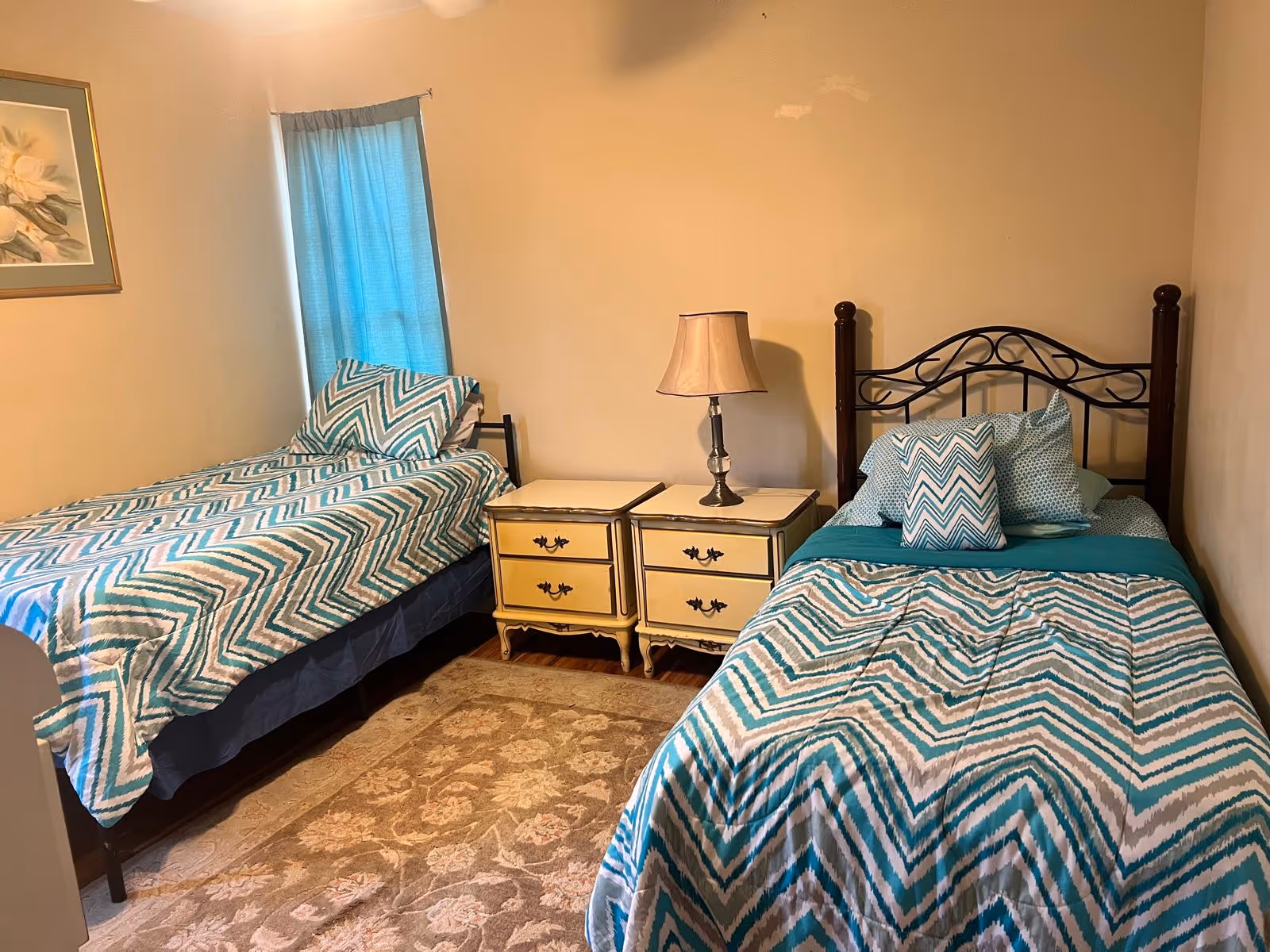Small bedroom with two twin beds in blue chevron bedding, a pair of nightstands and a lamp between them.