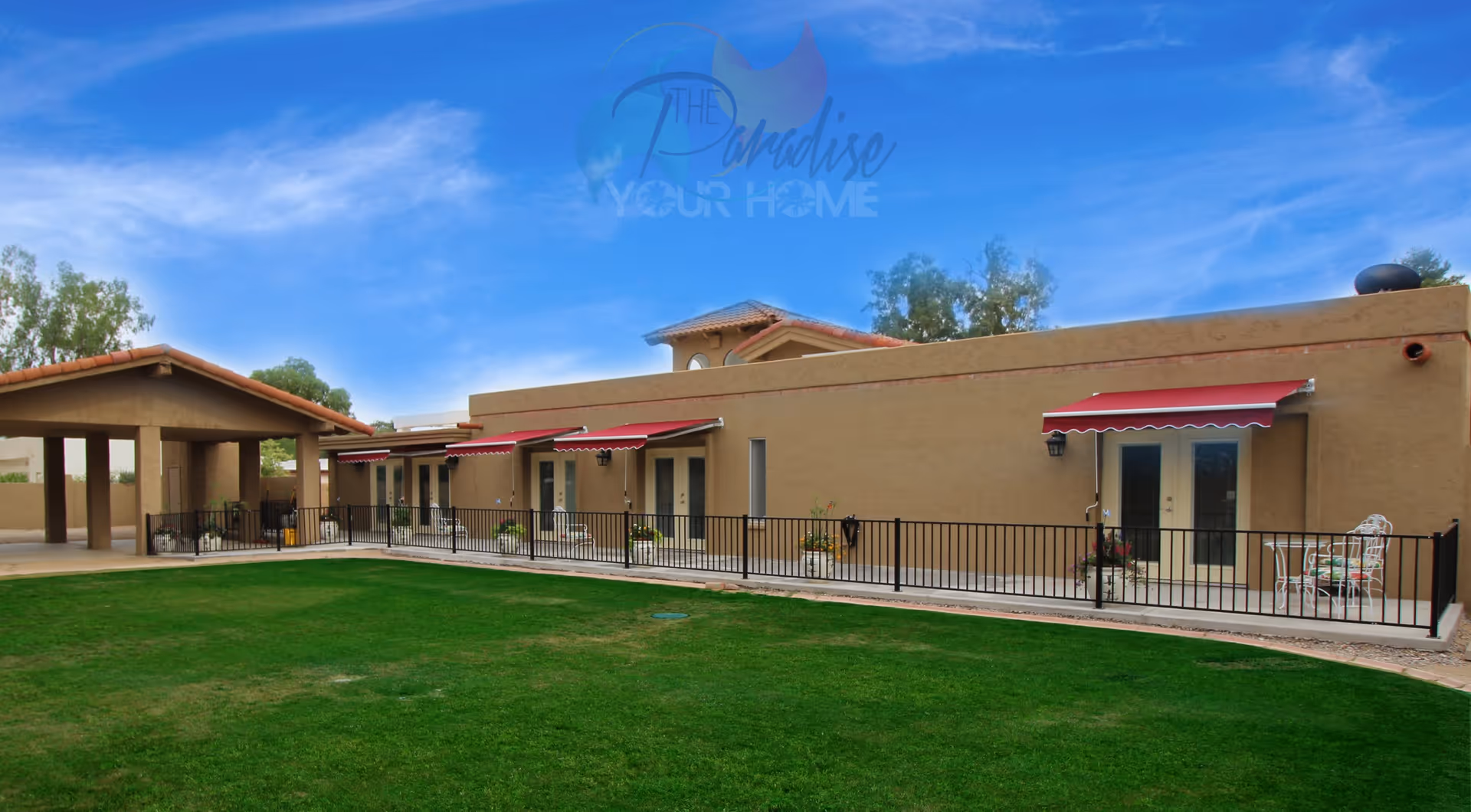 Exterior view of The Paradise Assisted Living Home featuring a single-story building with beige stucco walls and red awnings over several doors. There is a green lawn in the foreground and a covered entrance on the left side. The sky is clear and blue.