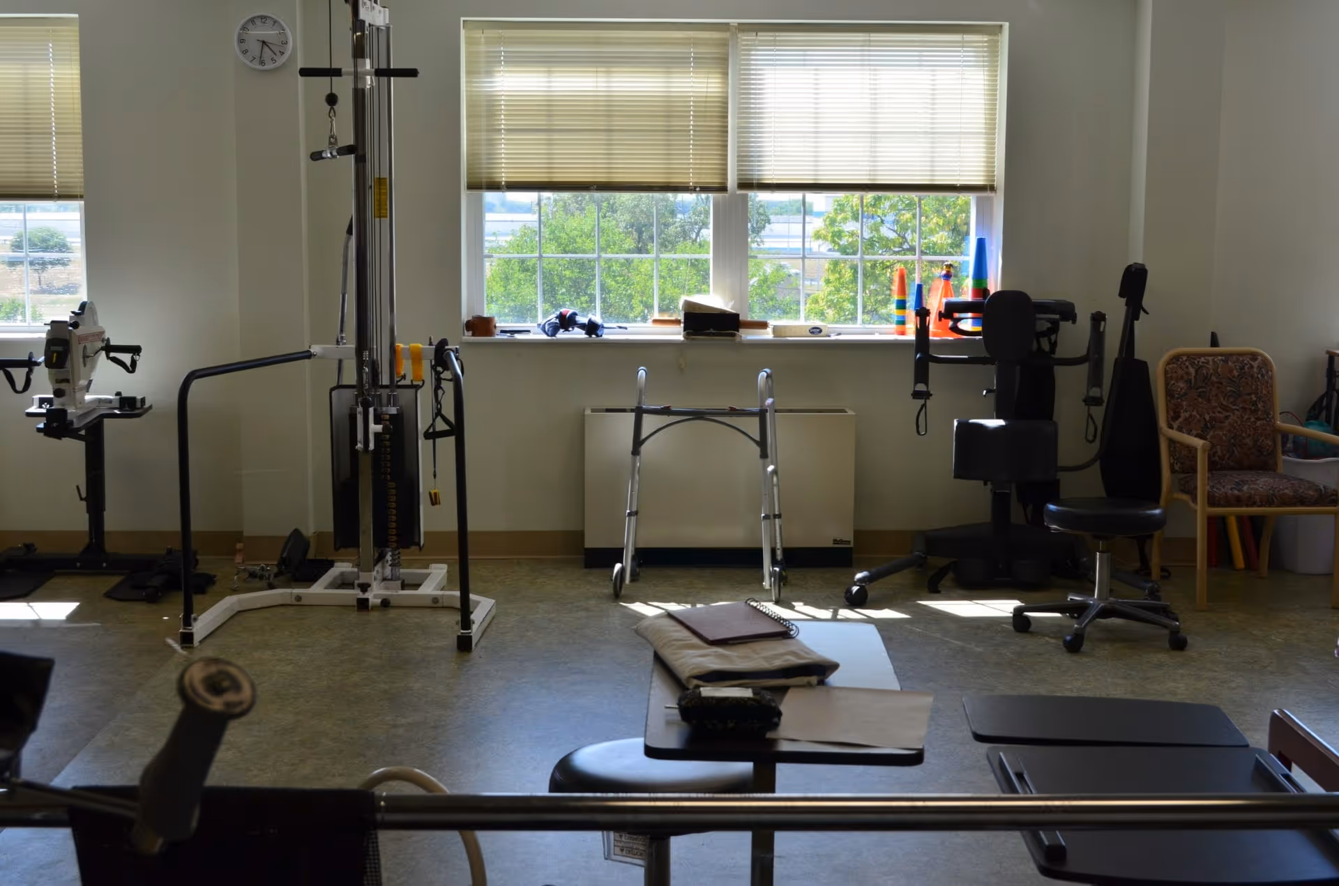 Interior rehabilitation/exercise room with windows, a walker, weight machines, chairs and therapy equipment.