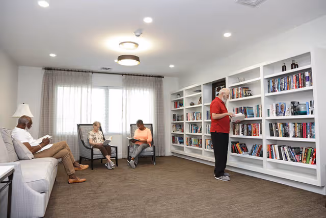 Four seniors reading in a well-lit common room with bookshelves along one wall.