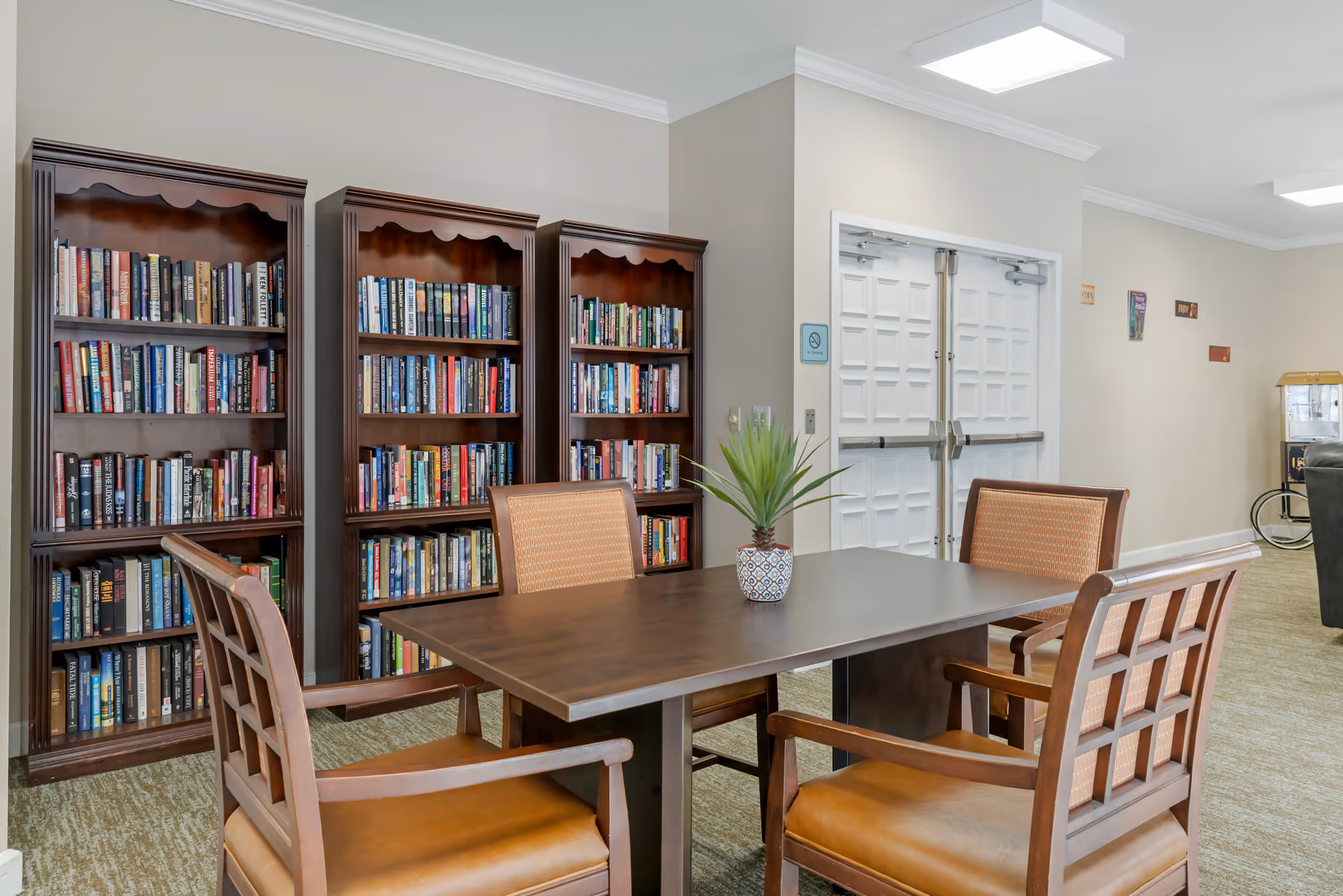 A seating area with a wooden table, four chairs, a small potted plant, and bookshelves filled with books against the wall.
