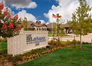 Exterior view of Larkspur senior living with brick sign, flag, and landscaped lawn