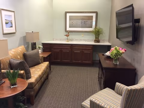 A cozy sitting area with a sofa, striped armchair, wall-mounted TV, and cabinetry with a countertop and decorative accents.