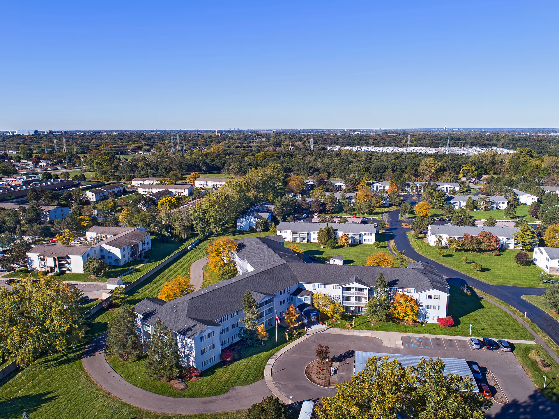 Aerial view of American House Sterling Meadows senior living facility surrounded by green lawns, trees, and multiple residential buildings under a clear blue sky.