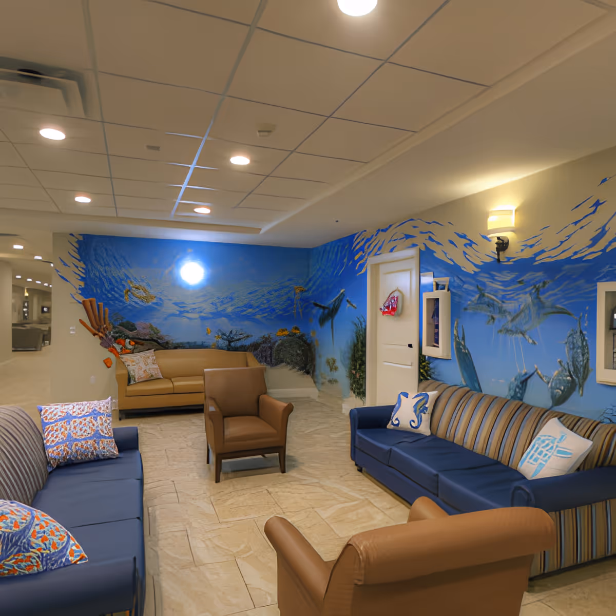Comfortable lounge with sofas and armchairs in front of a blue underwater mural.