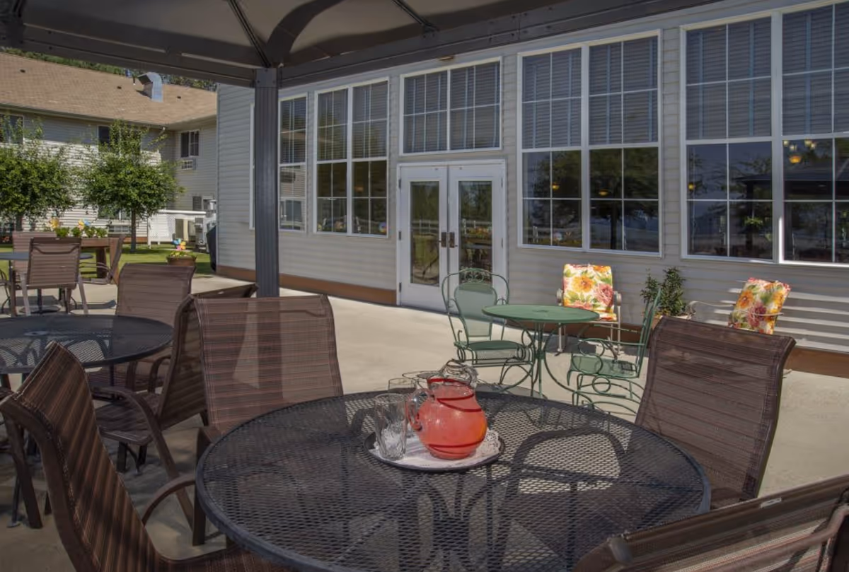 Outdoor patio with metal tables and chairs beside a building with large windows.