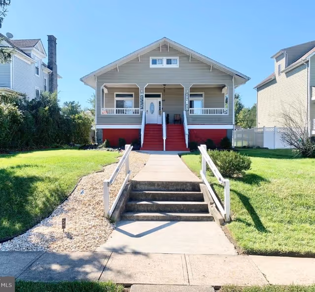 Front exterior of a bungalow-style house with red stairs, a covered porch, and a concrete walkway leading up to it.