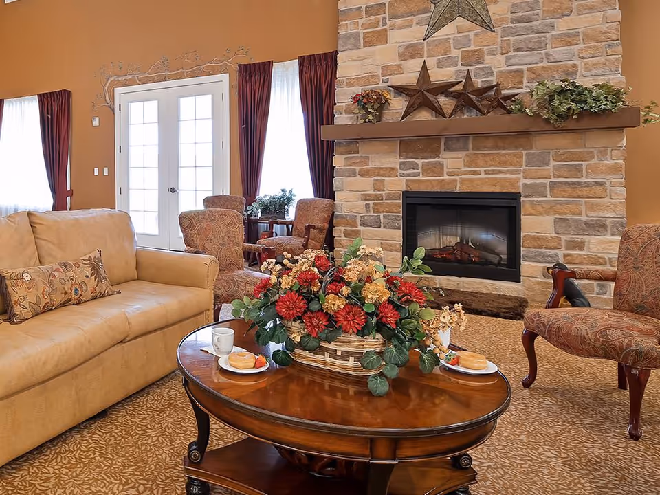 Cozy living room with a stone fireplace, sofa and armchairs arranged around a coffee table topped with a floral centerpiece.