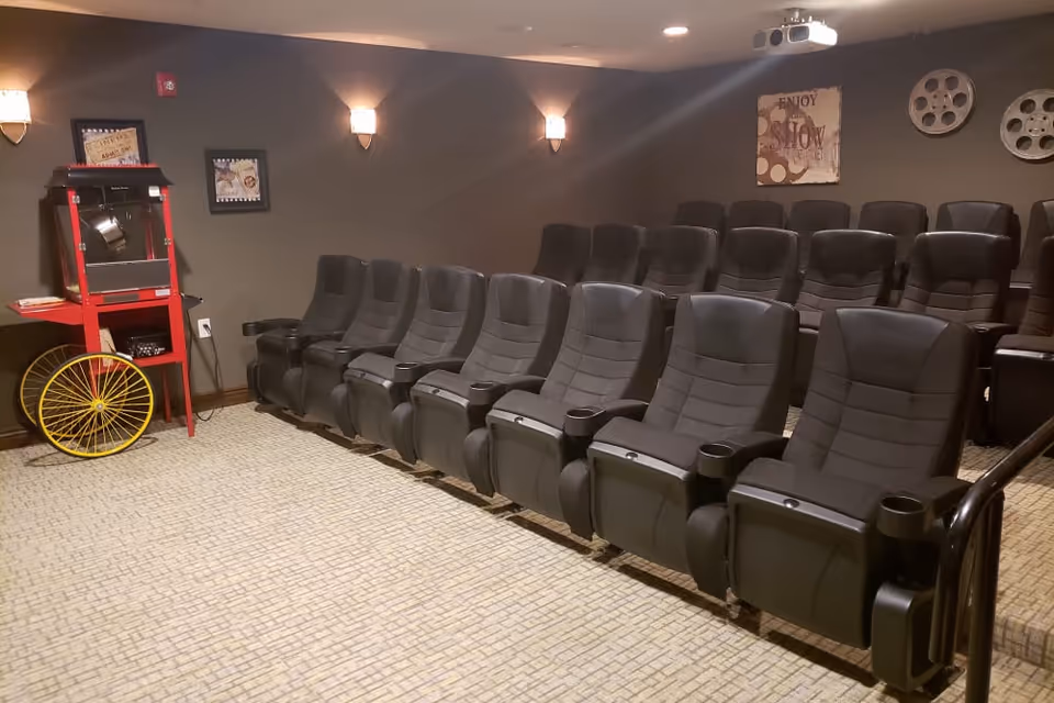 Small movie theater screening room with rows of black reclining seats, a popcorn machine, and film-themed wall decor.