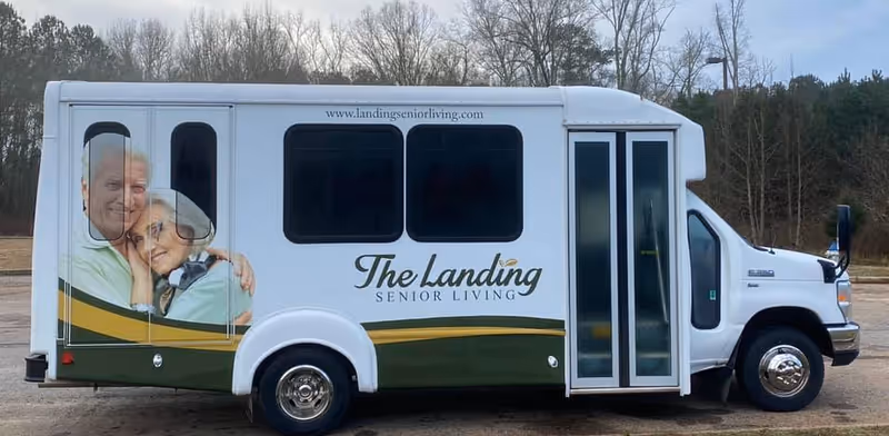 White shuttle bus for The Landing Senior Living with a large mural on the side.