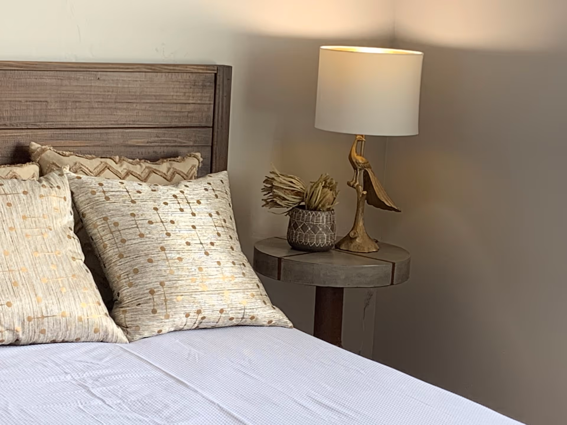 Wooden bed with patterned pillows and a bedside table holding a lamp and decorative vase.